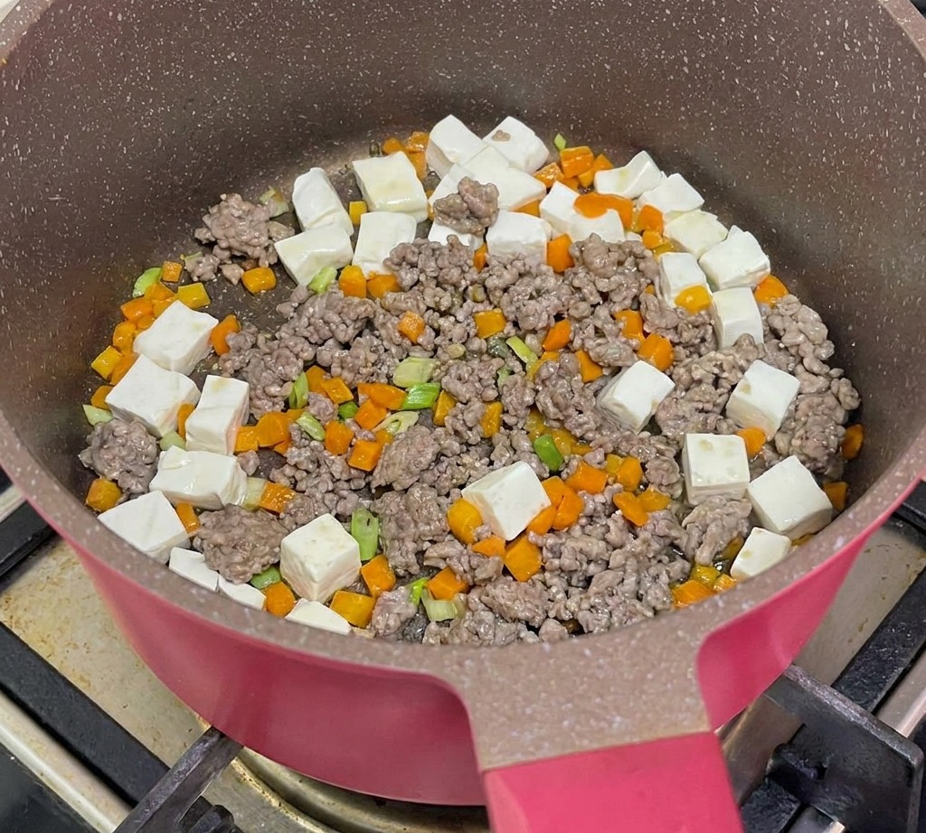 Eau bouillante versée dans la poêle contenant le tofu, le bœuf et les carottes pour laisser mijoter.