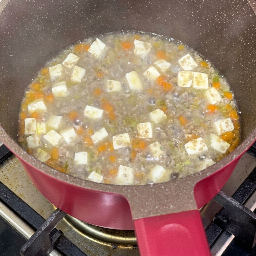 Sauce soja ajoutée à un mélange mijotant de bœuf haché, tofu et carottes.