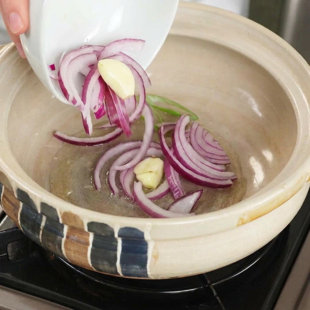 Oignons rouges et ail dans un pot dargile chaud avec de lhuile.