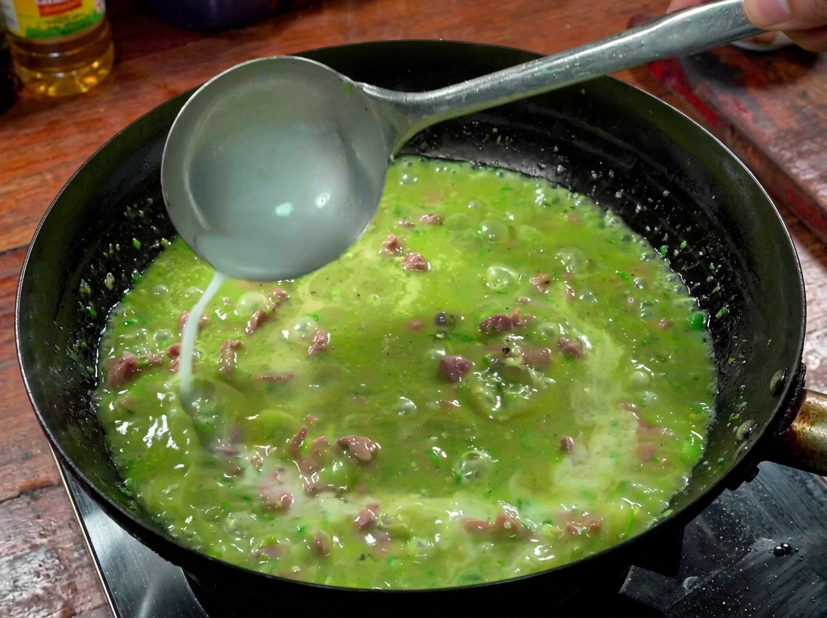 Une louche versant un mélange deau et damidon dans le bouillon épicé qui bout dans un wok.