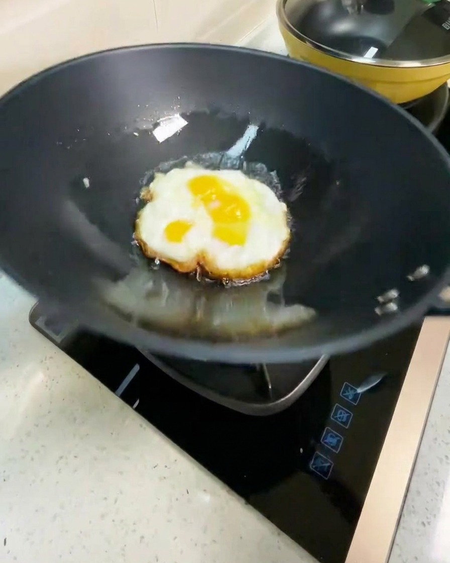 Œuf frit retourné dans un wok chaud, montrant une face brune dorée.