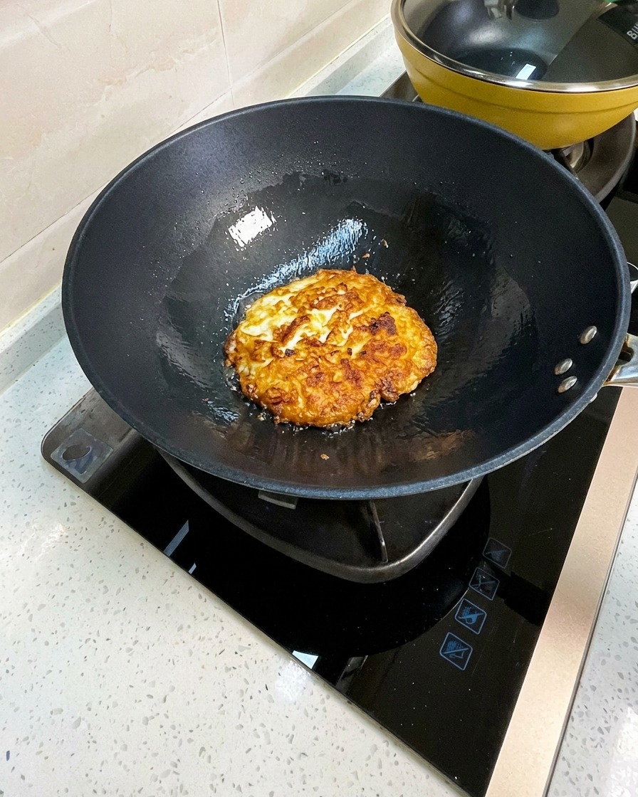 Œufs frits dans un wok cassés en gros morceaux avec une spatule en métal.