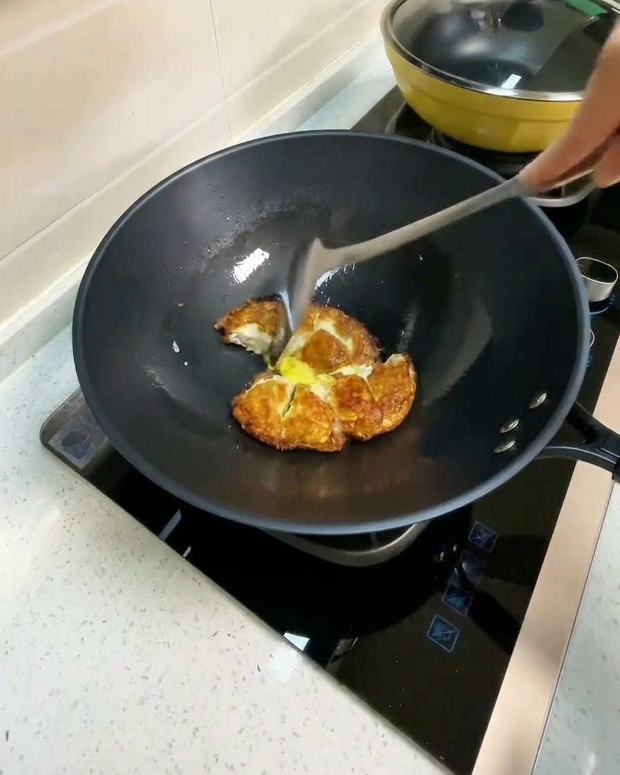 Eau chaude versée dans un wok contenant les morceaux dœufs frits.