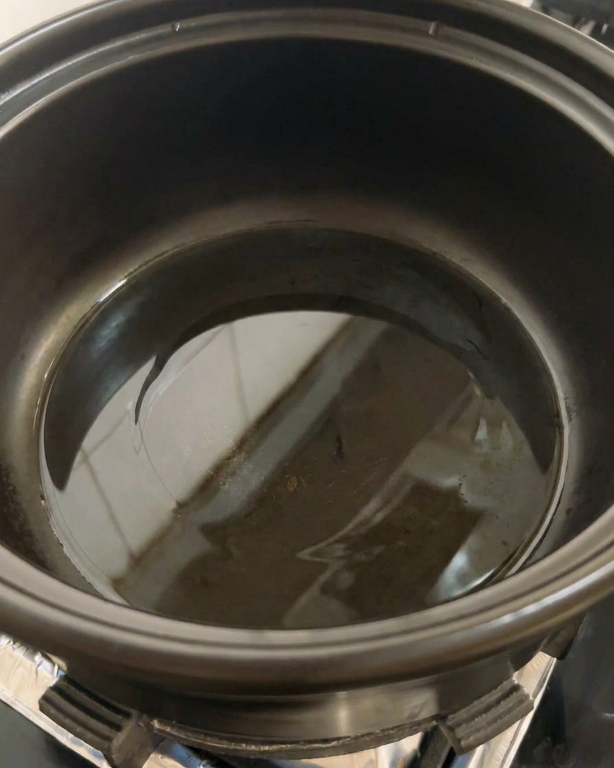 Une marmite noire sur une plaque de cuisson avec un filet dhuile commençant à chauffer au fond.