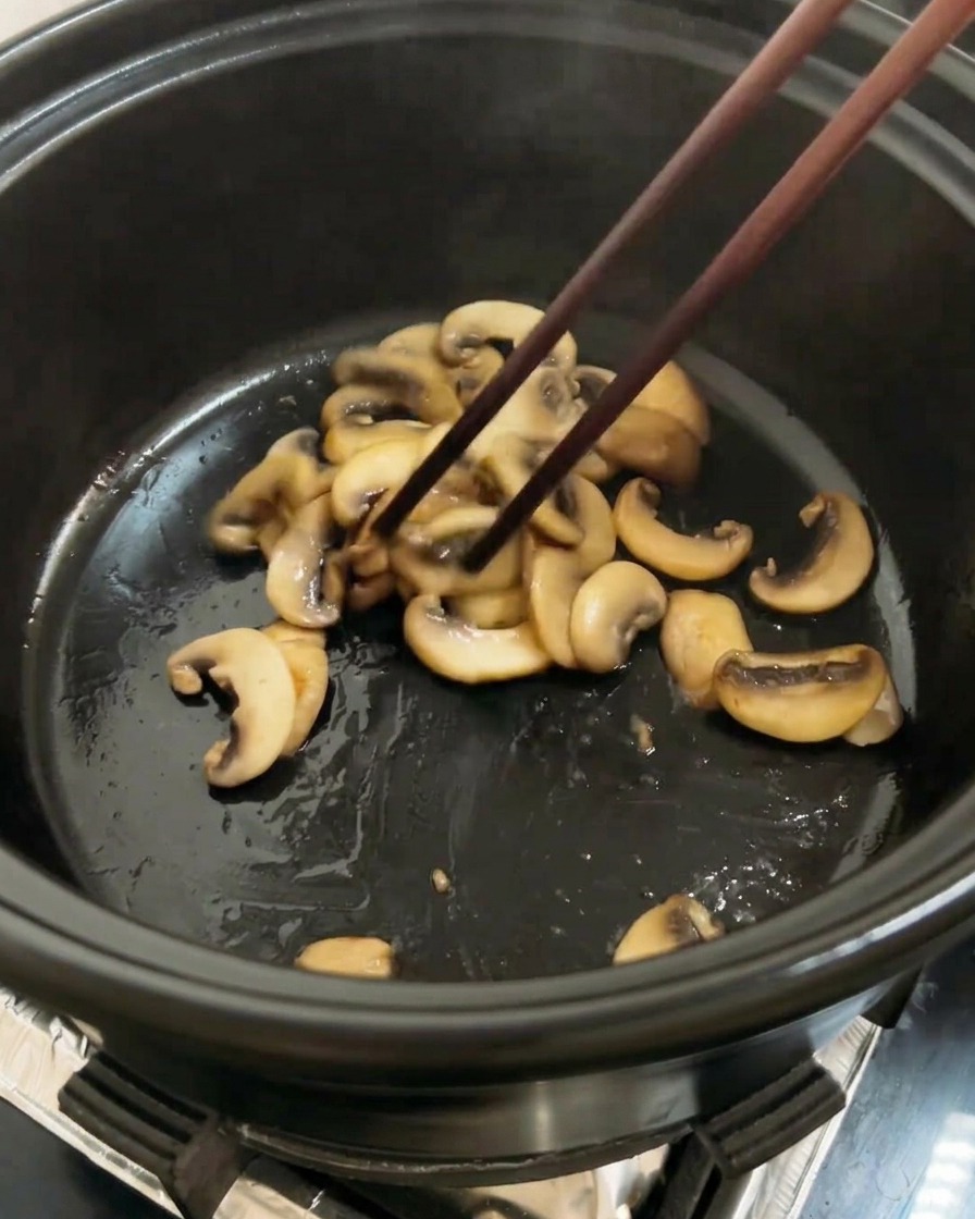 Tomates rouges hachées ajoutées dans la marmite aux côtés des champignons dorés, prêtes à être sautées.