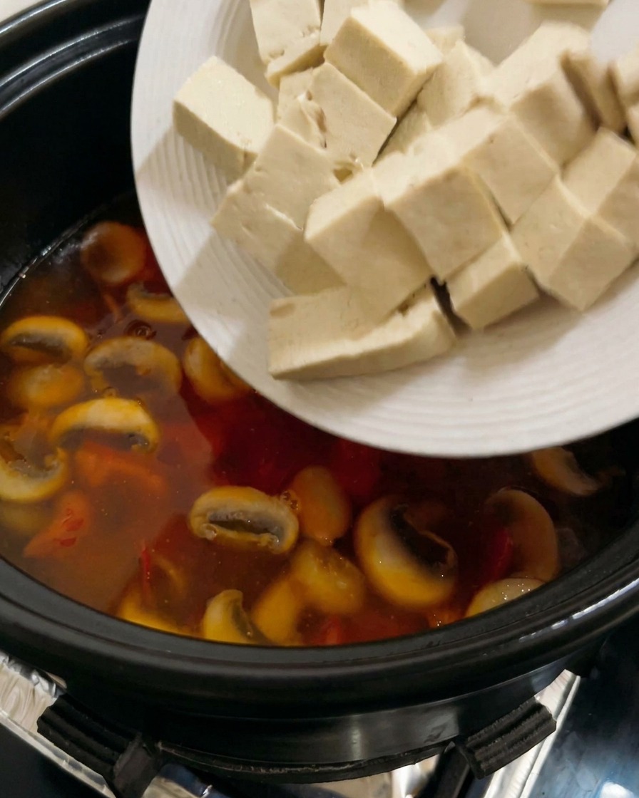 Cubes de tofu ferme blanc ajoutés à une soupe tomate-champignon frémissante.