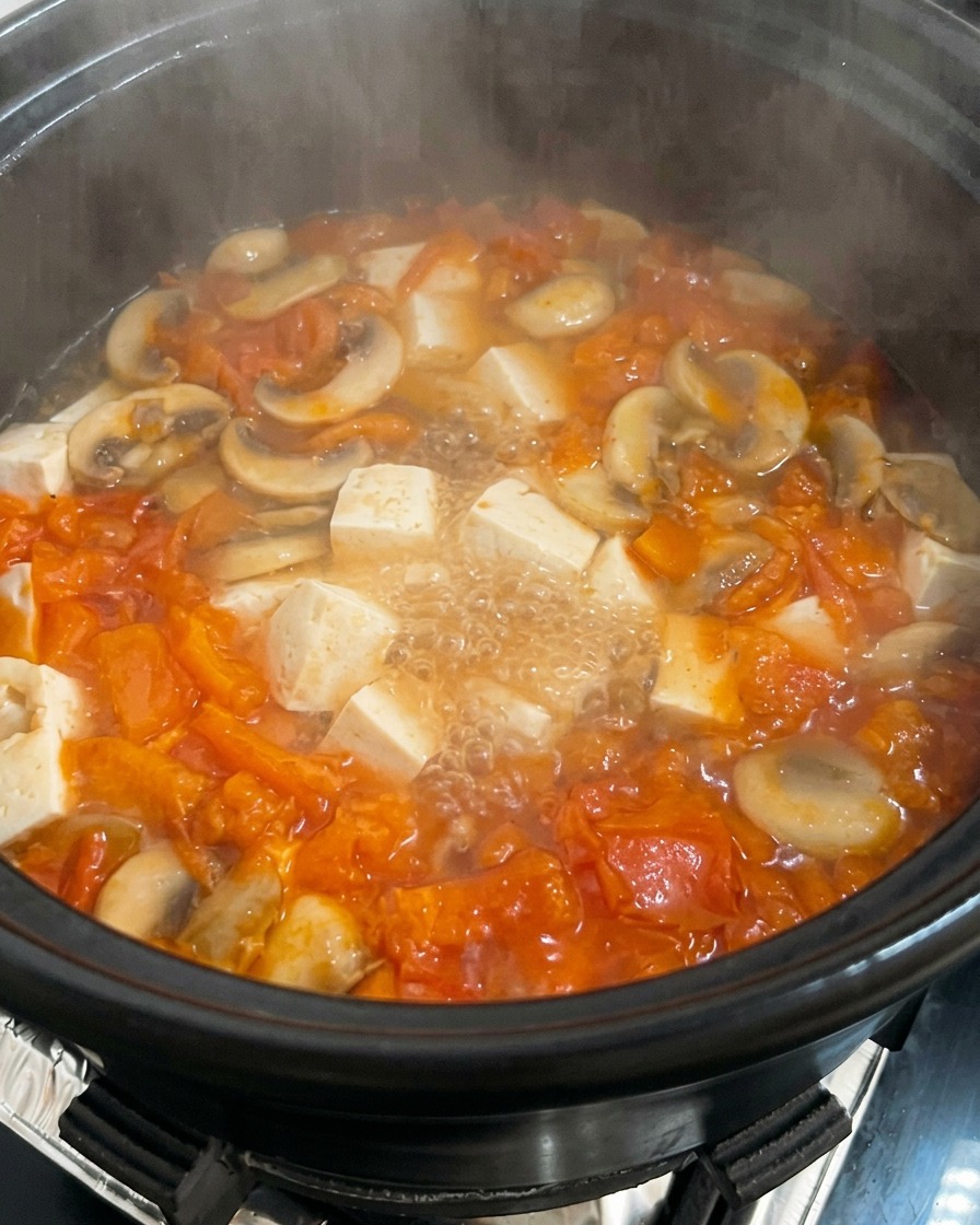 Marmite de soupe tomate-champignon avec tofu, dans laquelle on verse un œuf battu.