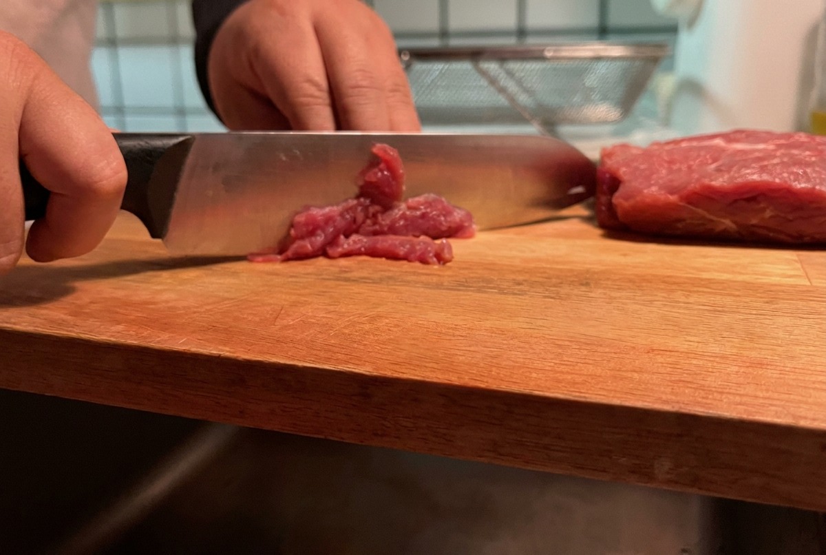 Porc maigre coupé en fines lamelles sur une planche à découper en bois.