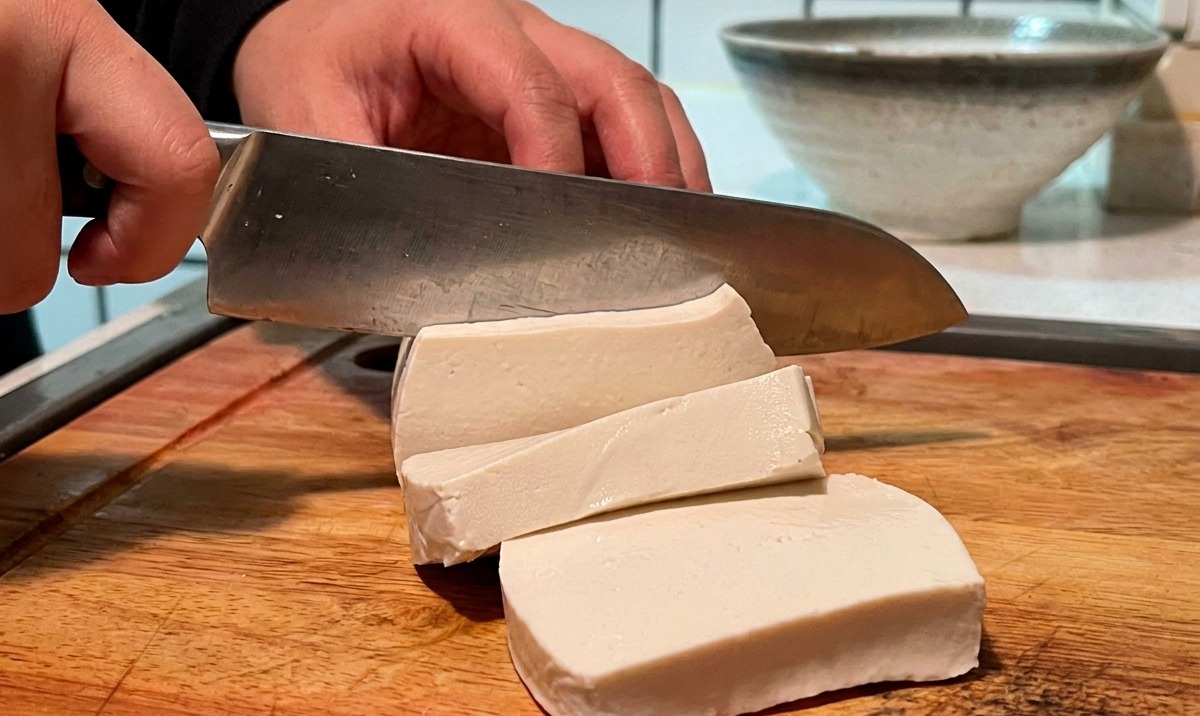Un bloc de tofu blanc coupé en petits cubes sur une planche en bois.
