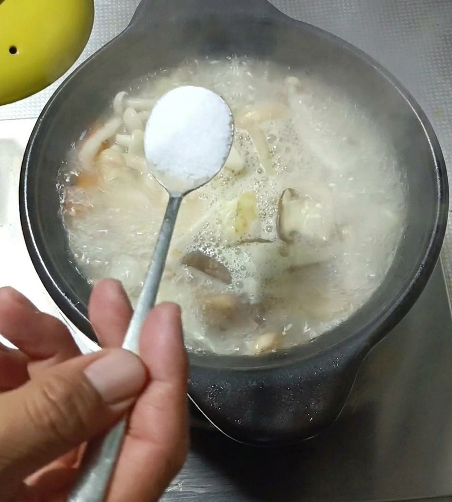 Gros plan sur une cuillère dassaisonnement versée dans une soupe de champignons et dœufs bouillonnante.