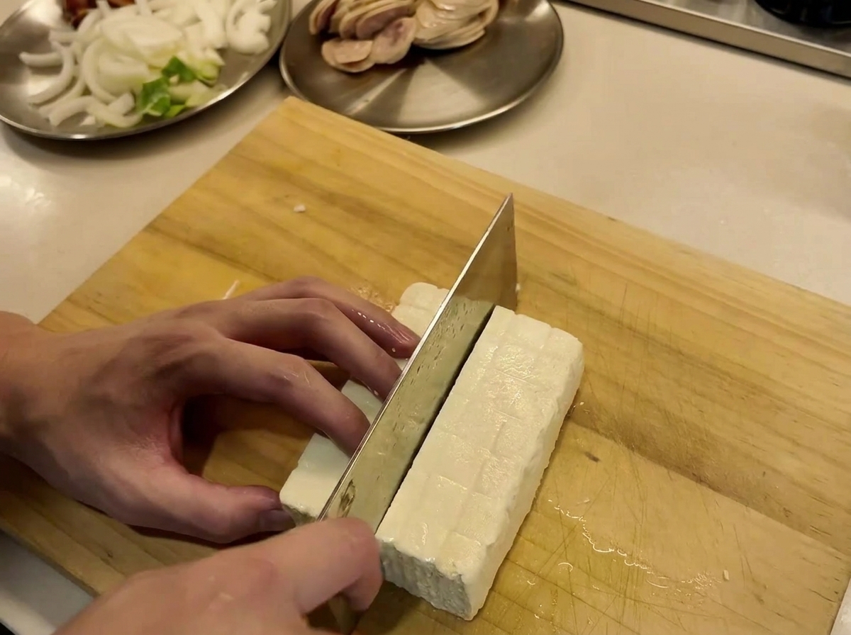 Bloc de tofu en train dêtre coupé en tranches nettes sur une planche à découper en bois.
