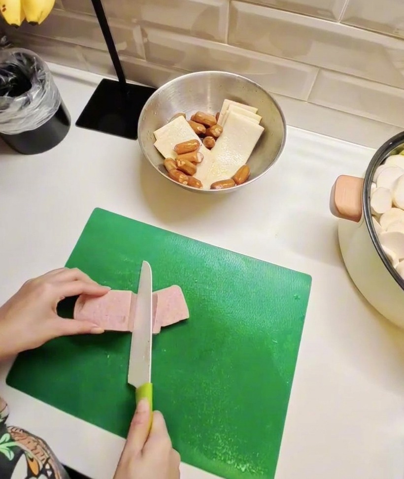 Tranches de viande en conserve et de gâteaux de poisson sur une planche, montrant la préparation des ingrédients principaux.