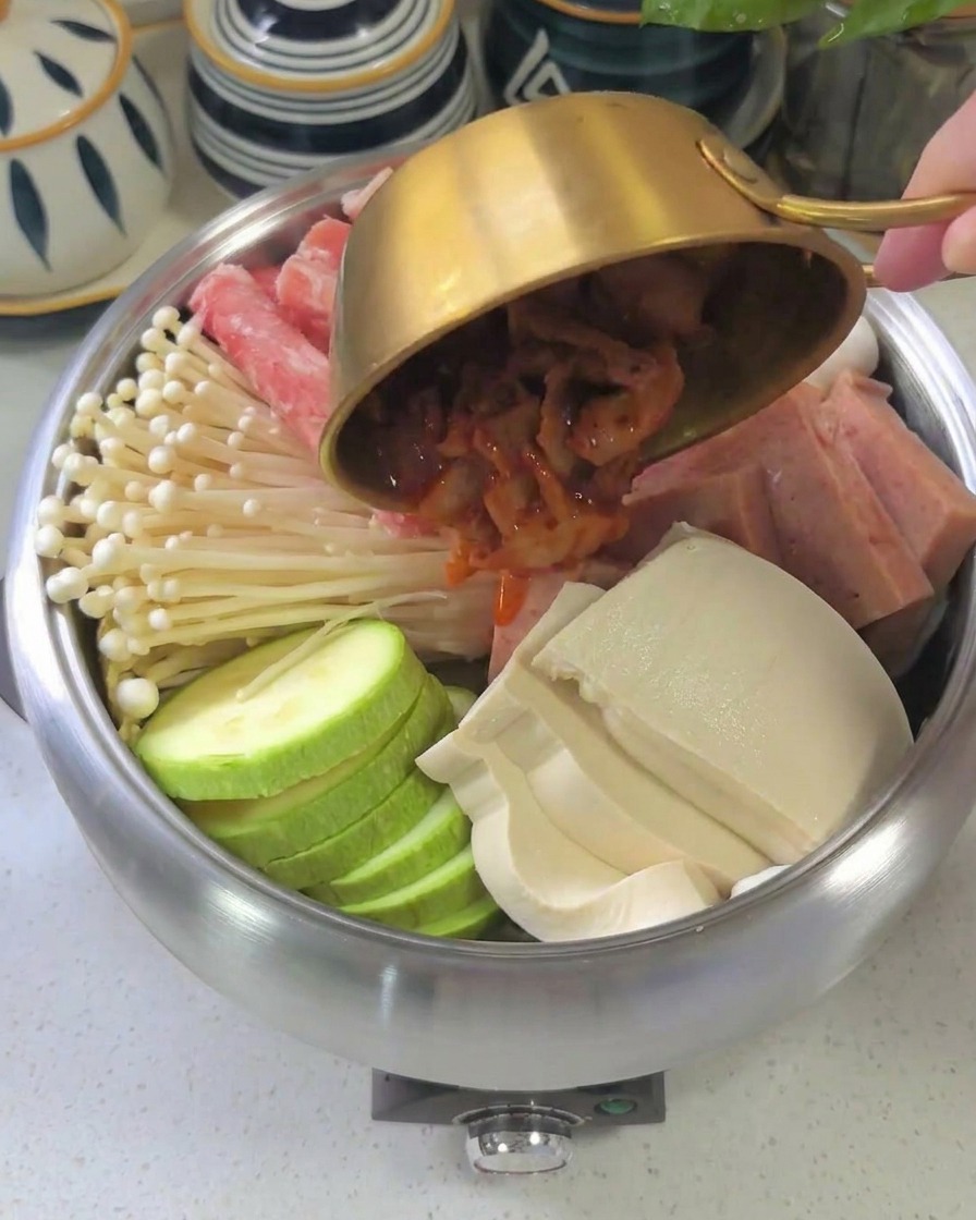 La sauce rouge épaisse étant versée dun bol sur les ingrédients arrangés dans la marmite.