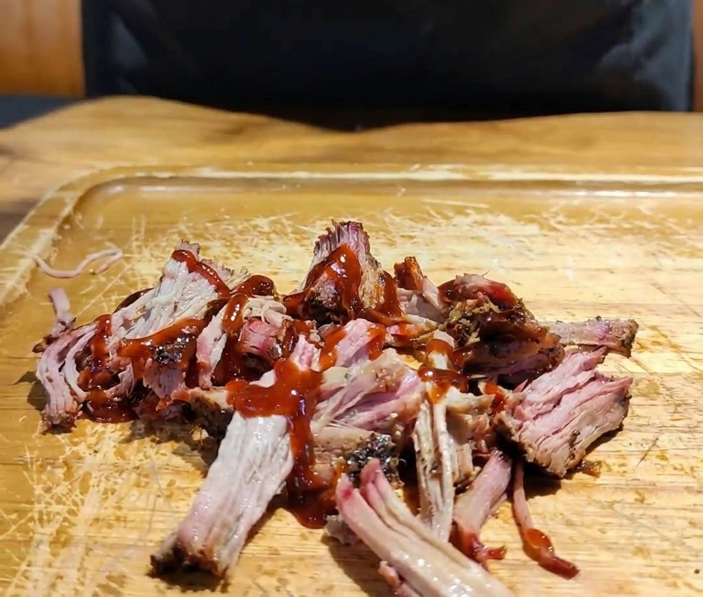 Une main dépose un mélange de chou blanc et rouge râpé sur le porc effiloché en sauce sur une planche.