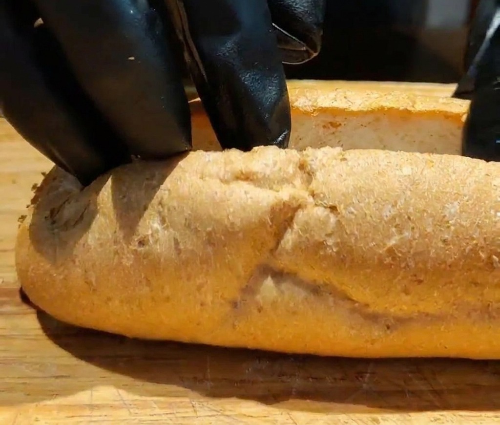 Gros plan de mains ouvrant une baguette de blé entier tranchée pour créer de lespace pour la garniture.