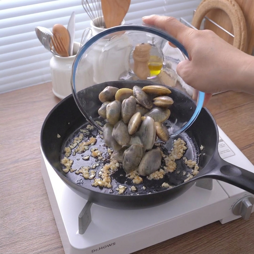 Un bol en verre versant des palourdes fraîches et fermées dans une poêle avec de lail haché sauté.