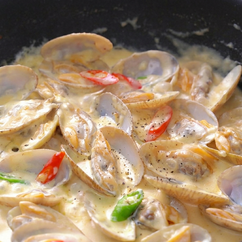 Gros plan de palourdes dans une sauce crémeuse épaisse, parsemées de poivre, de persil et de piments.