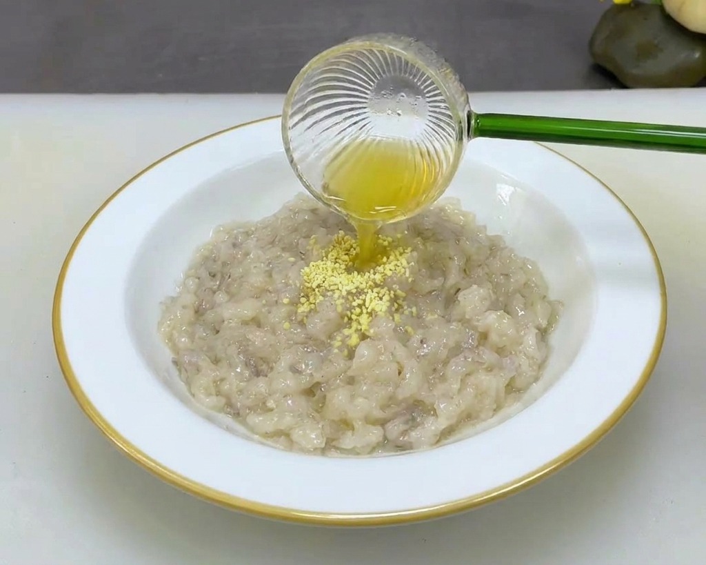 Une personne versant du bouillon de poulet en poudre dans un bol blanc rempli de pâte de crevettes épaisse.