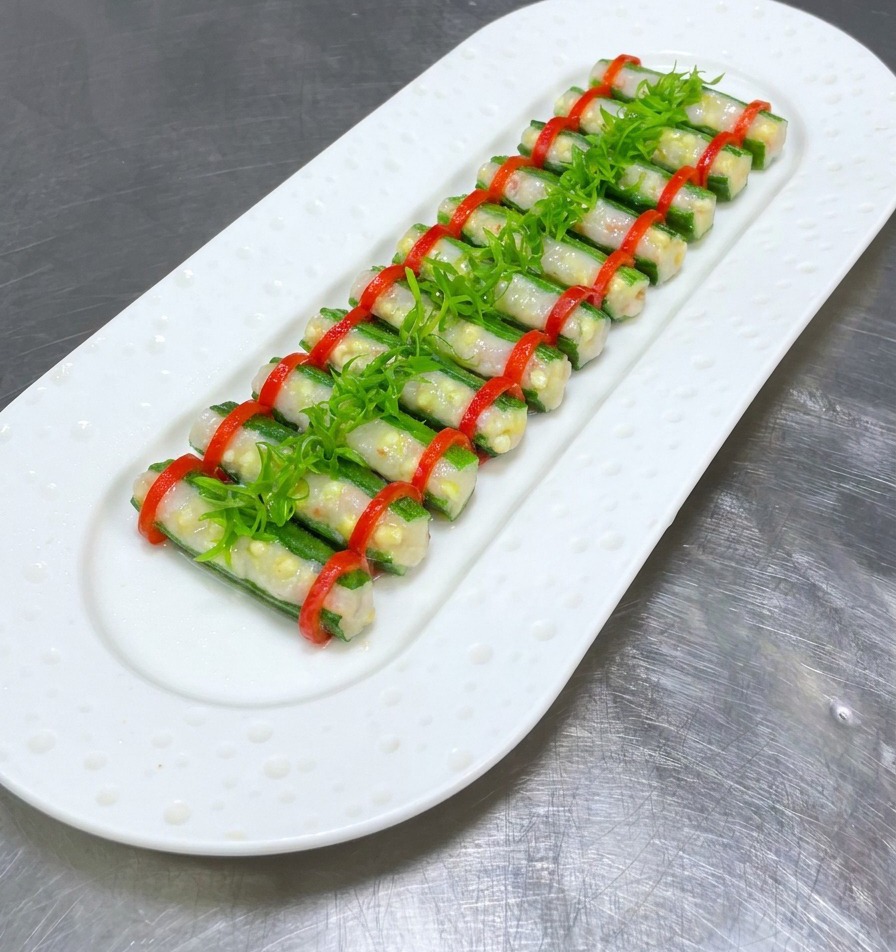 Gombos farcis cuits à la vapeur sur une assiette blanche, surmontés dune rangée centrale doignons verts émincés.