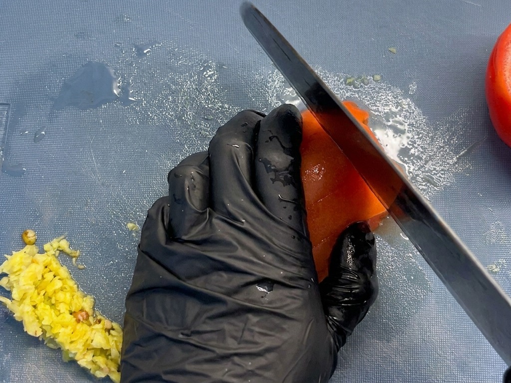 Gros plan dun chef coupant une tomate pelée en dés uniformes sur une planche à découper bleue.