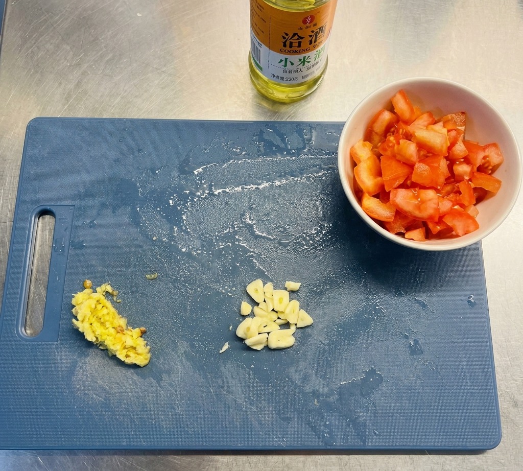 Une planche à découper bleue présentant de lail émincé, des piments hachés et des tomates en dés à côté dune bouteille dhuile.