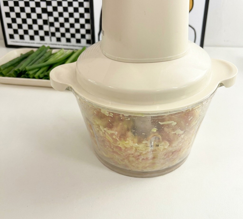 Un robot culinaire crème rempli dun mélange de poulet haché finement et de petites graines dokra jaunes.