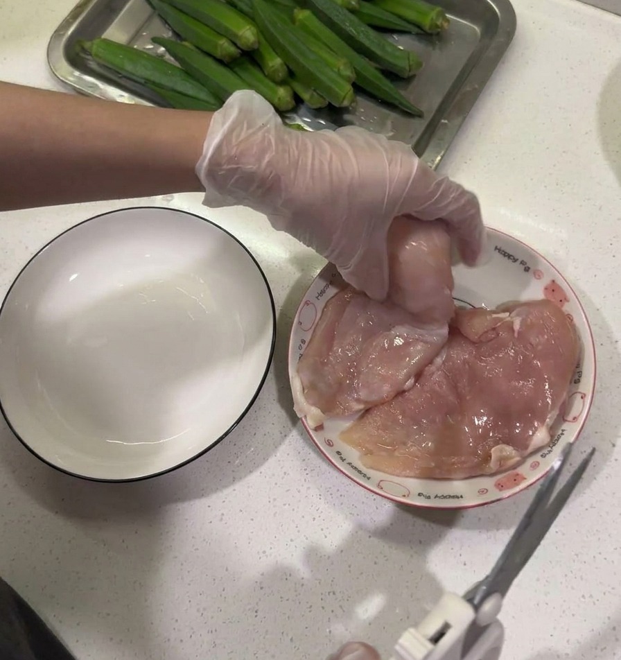 Ciseaux de cuisine utilisés pour retirer le gras dun blanc de poulet tenu au-dessus dune assiette.