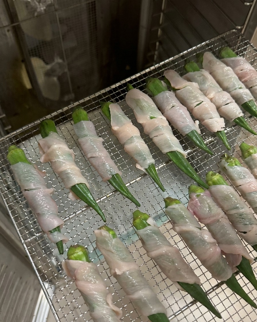 Rangées de gombos enroulés de poulet disposées sur une grille métallique à lintérieur dun déshydrateur en acier inoxydable.