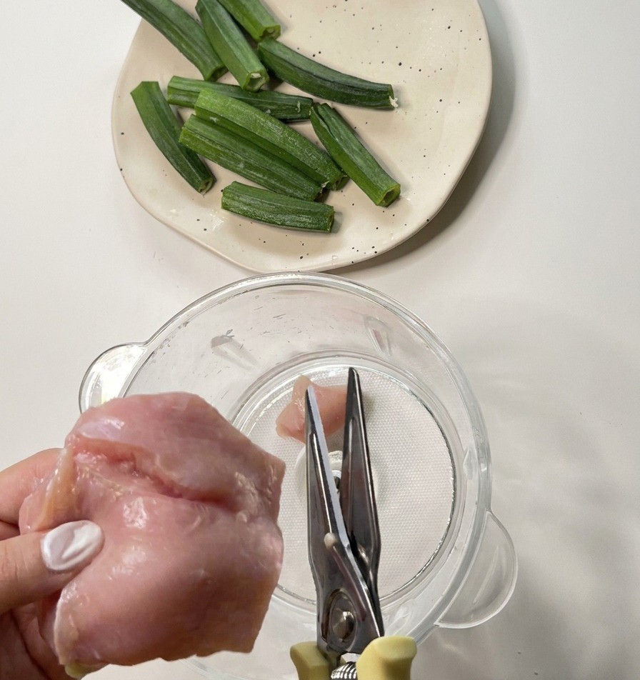 Utilisation de ciseaux de cuisine en métal pour couper du blanc de poulet cru dans le bol dun mixeur.