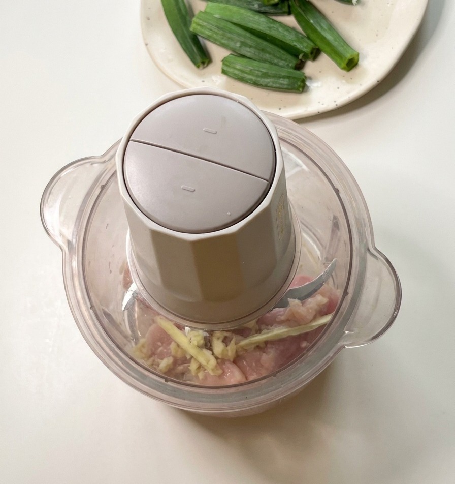 Un robot culinaire contenant des morceaux de poulet cru et des graines de gombo, prêt à être mixé.