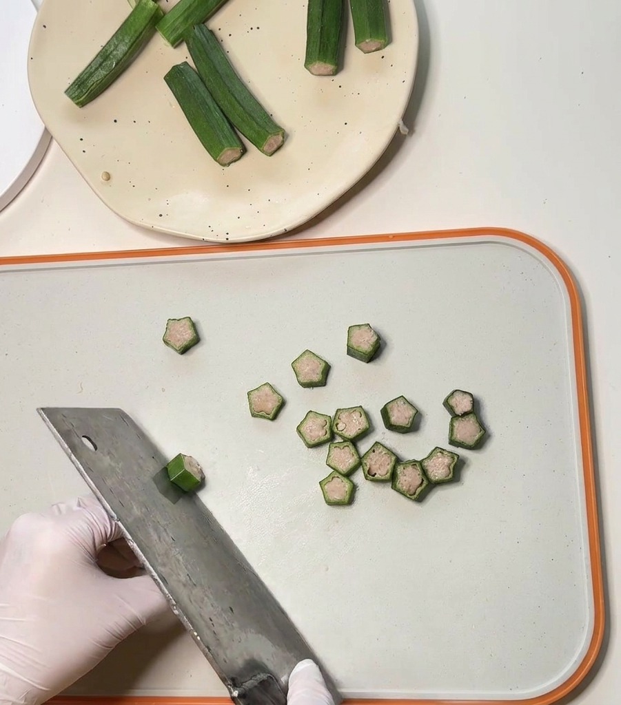 Un grand couperet en métal tranchant des gousses de gombo farcies en petites rondelles en forme détoile.