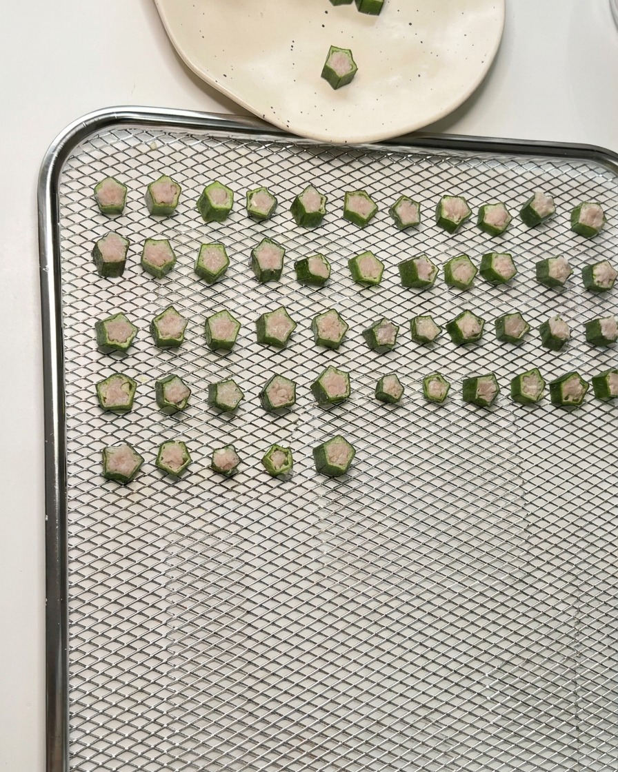 Des dizaines de friandises en forme détoile au gombo et au poulet disposées en rangées sur la grille dun déshydrateur.