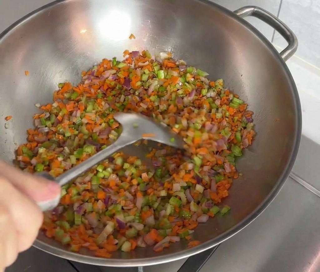 Mélange coloré de carottes, céleri et oignons rouges sautés à la spatule dans un wok en inox.