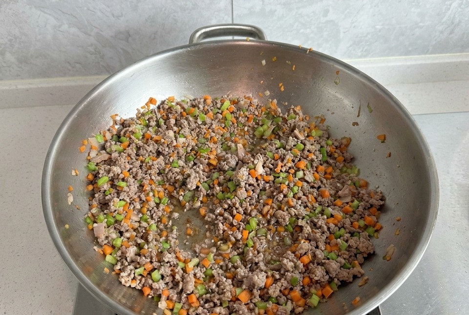 Viande hachée sautée avec des carottes et du céleri dans un grand wok en argent.