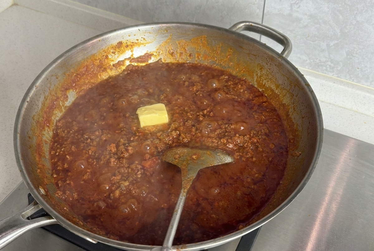 Un carré de beurre jaune posé sur la surface dune sauce tomate à la viande frémissante dans une grande poêle.