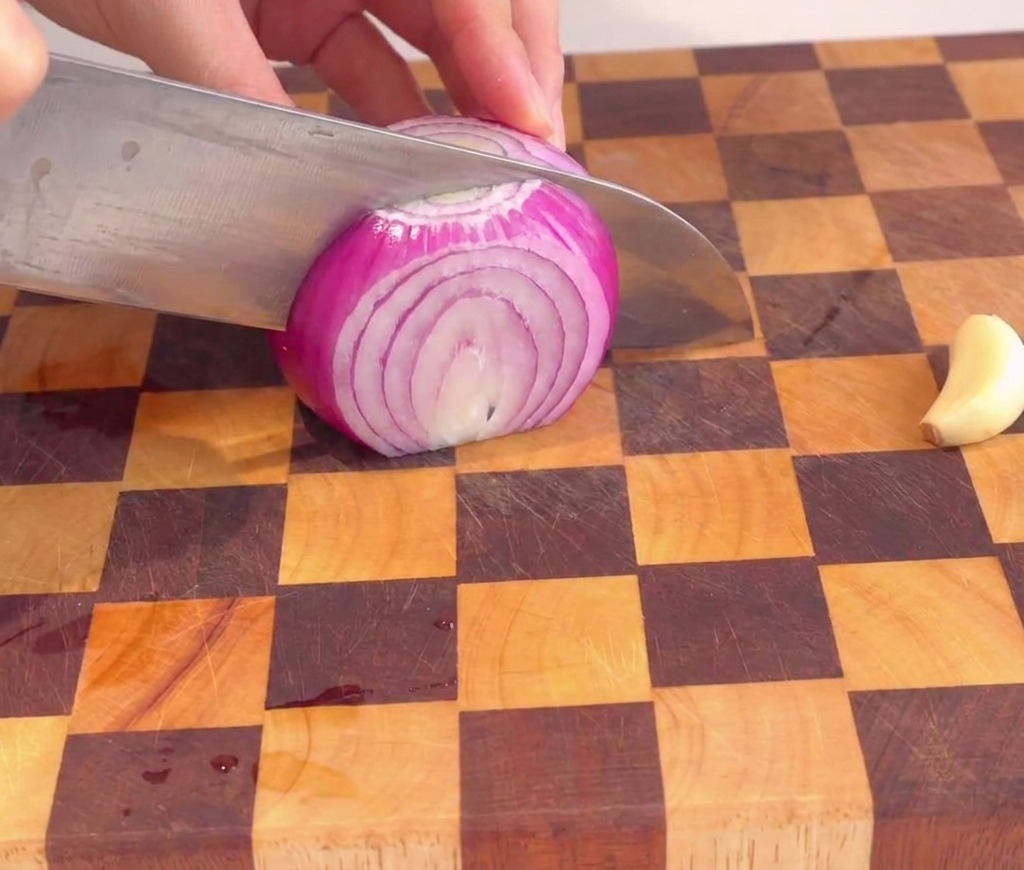 Une personne coupant finement un oignon rouge en petits dés uniformes sur une planche à découper en bois.