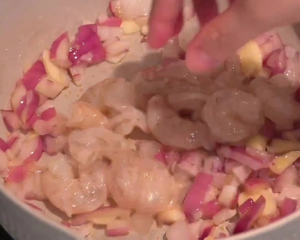 Crevettes crues ajoutées dans une poêle avec des oignons rouges et de lail sauté.