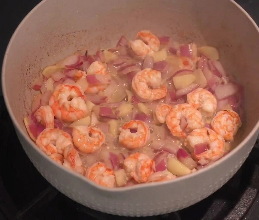 Crevettes sautées avec des oignons et de lail dans une grande poêle avec de la sauce rouge.