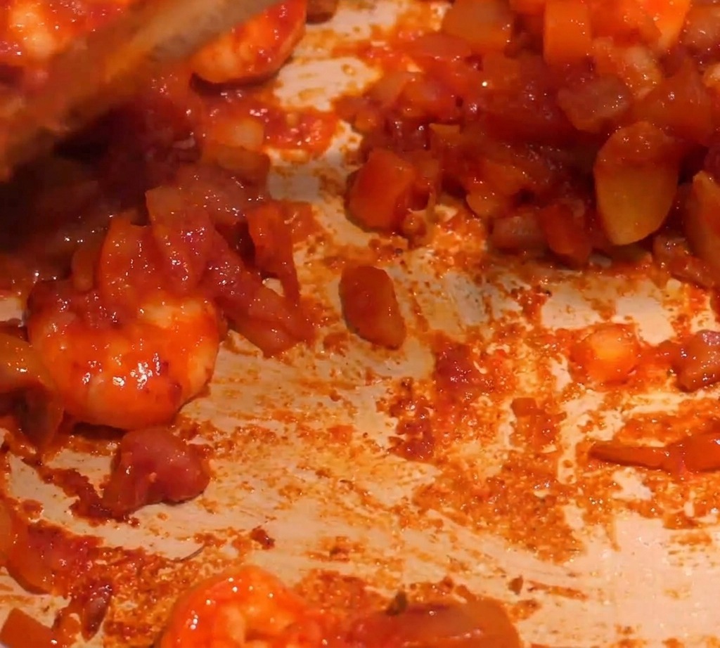 Une sauce rouge épaisse aux crevettes remuée dans une poêle pendant lajout de liquide.