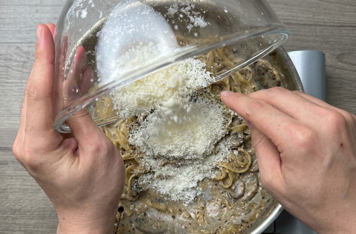 Gros plan des spaghettis finis mélangés vigoureusement dans la poêle pour créer une sauce brillante.