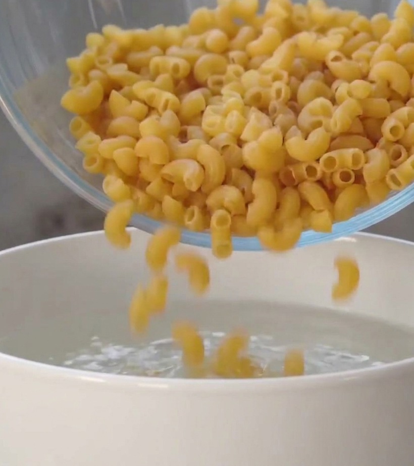Des pâtes spirales sèches tombant dun bol en verre dans une casserole deau bouillante