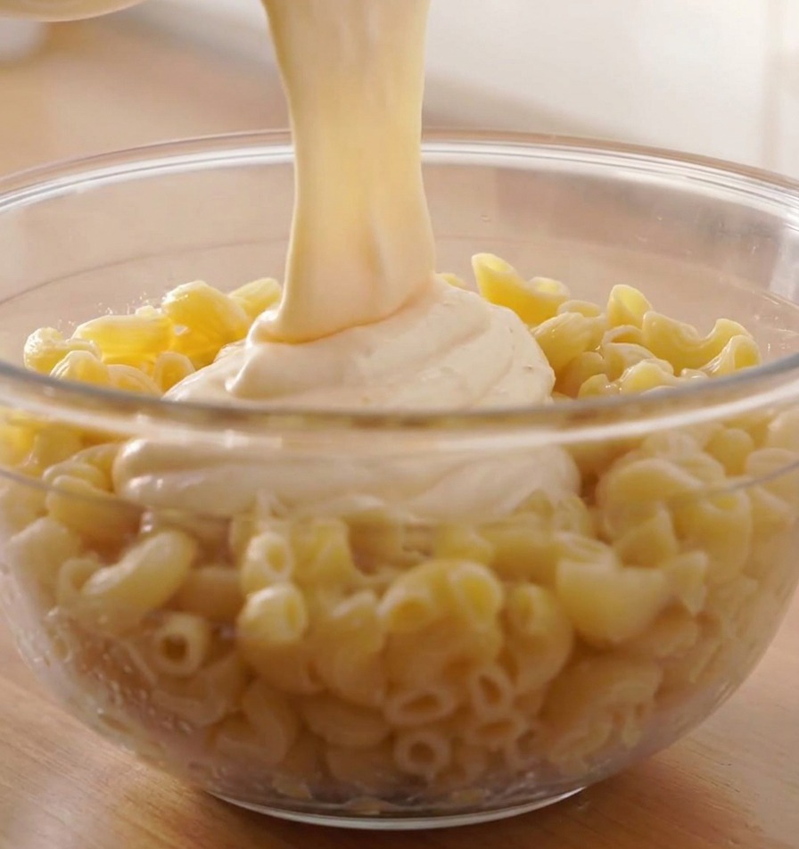 Une sauce au fromage fondue versée sur un grand bol de pâtes spirales cuites