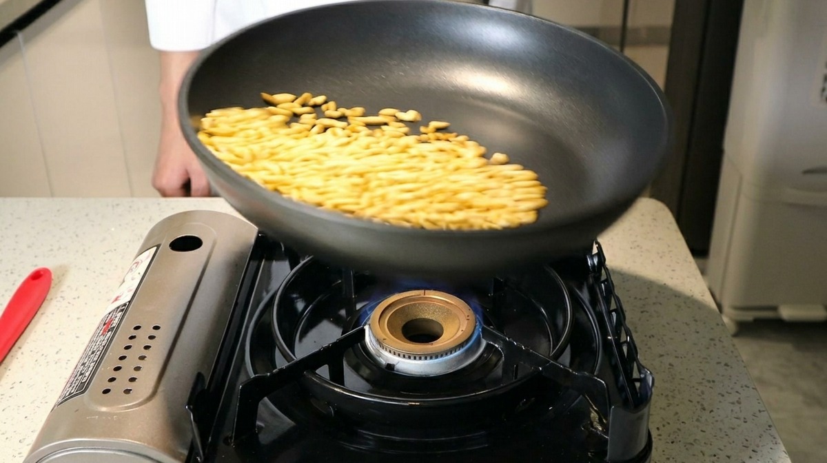 Pignons de pin sautés dans une poêle antiadhésive noire sur une flamme de gaz bleue.