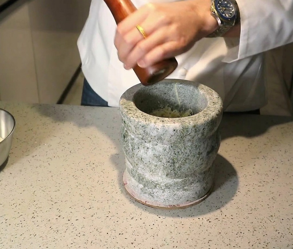 Un moulin à poivre en bois utilisé au-dessus des ingrédients dans un mortier en pierre.