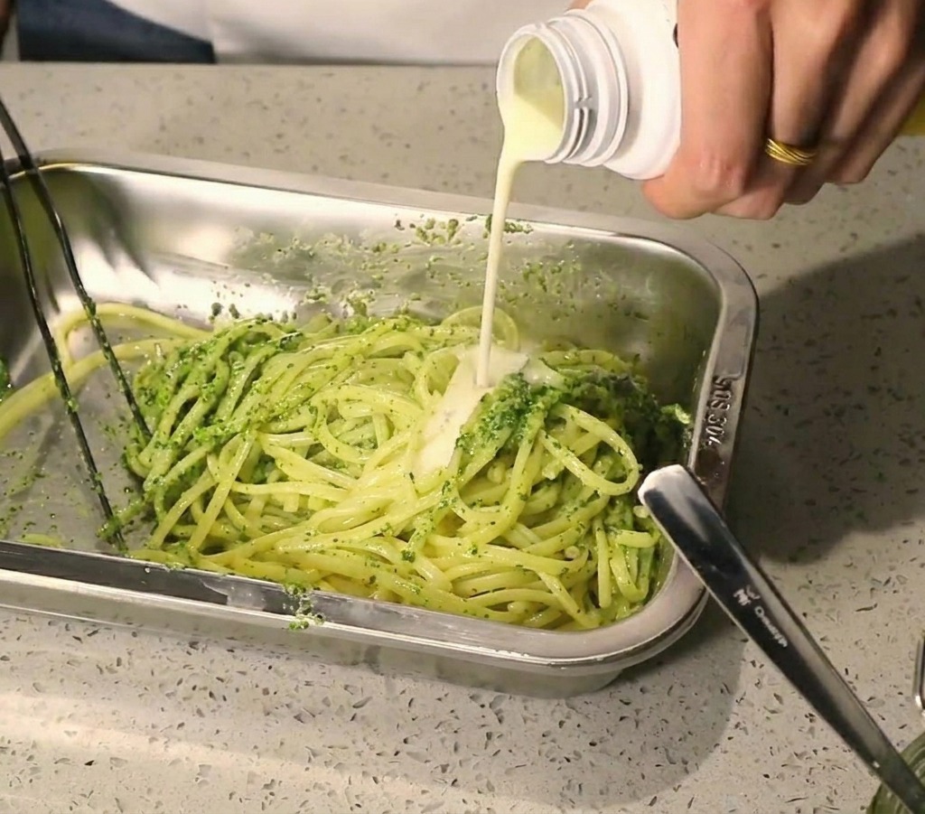 Filet de sauce crémeuse blanche versé sur des pâtes garnies de pesto vert.
