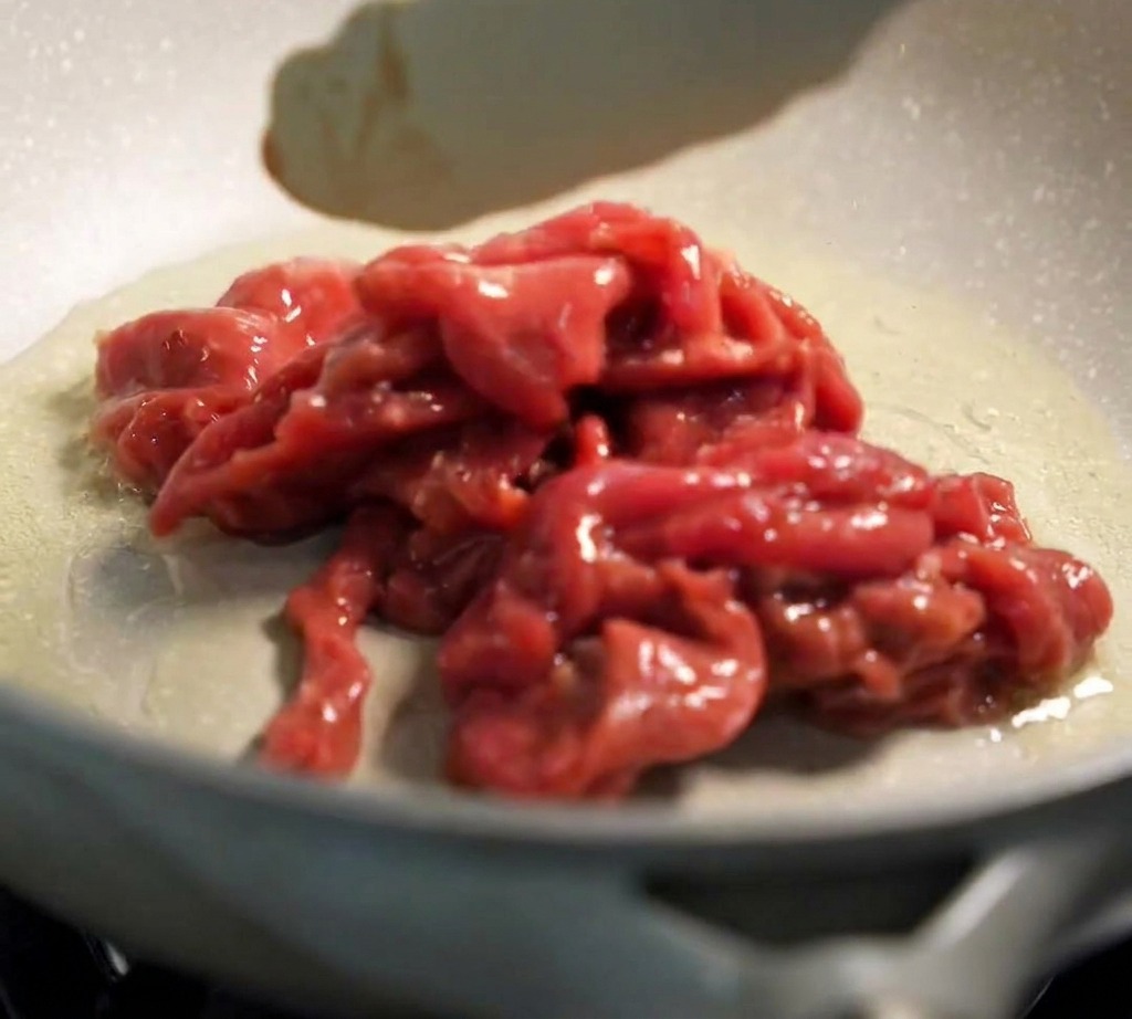 Une pince déposant du bœuf mariné dans une poêle chaude et huilée.
