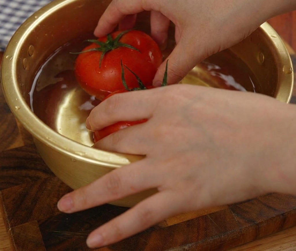 Deux tomates rouges entières congelées plongées dans un bol en métal doré rempli deau.
