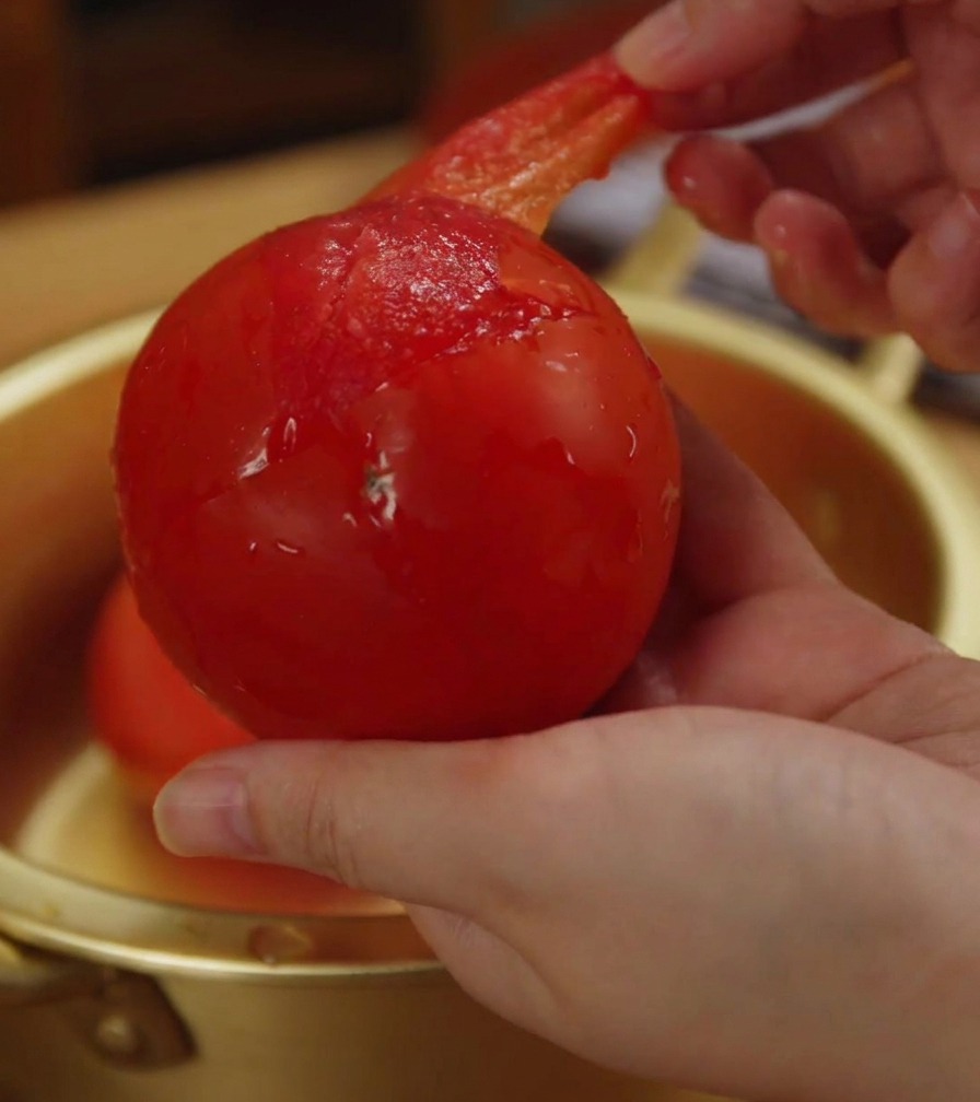 Gros plan dune main retirant la peau fine et translucide dune tomate ramollie.