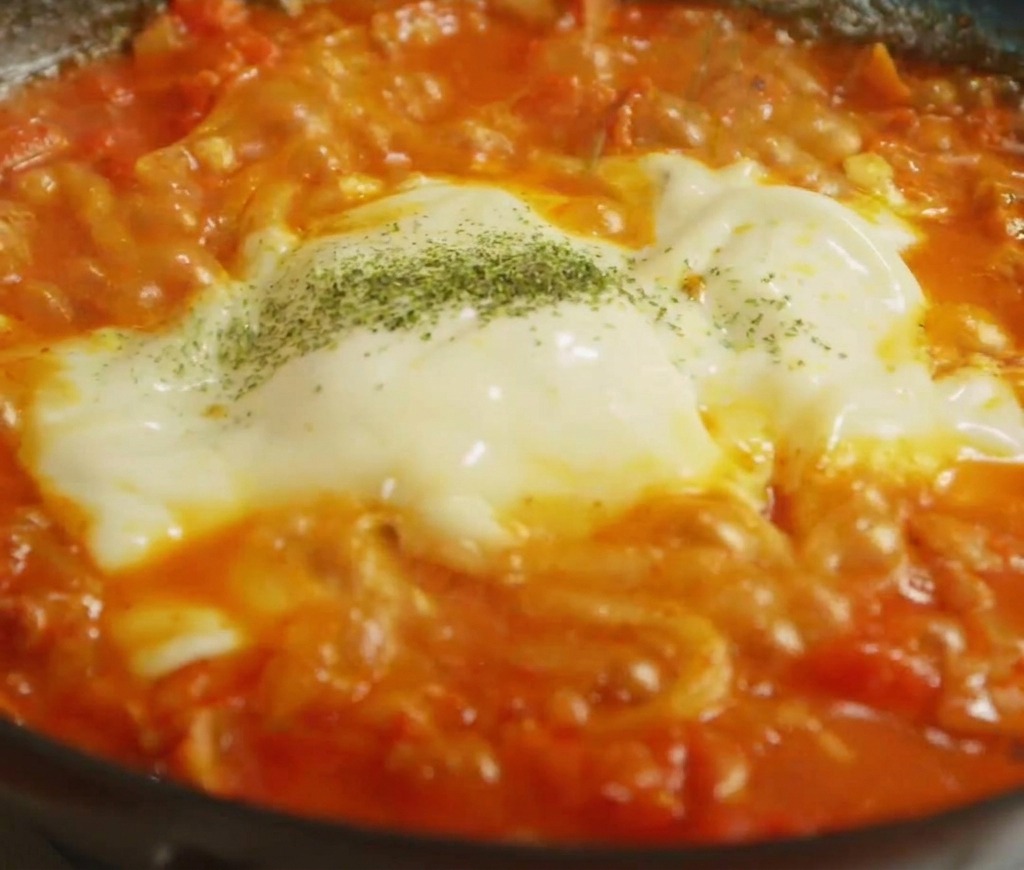 Herbes séchées saupoudrées sur une couche de fromage fondu recouvrant des nouilles.