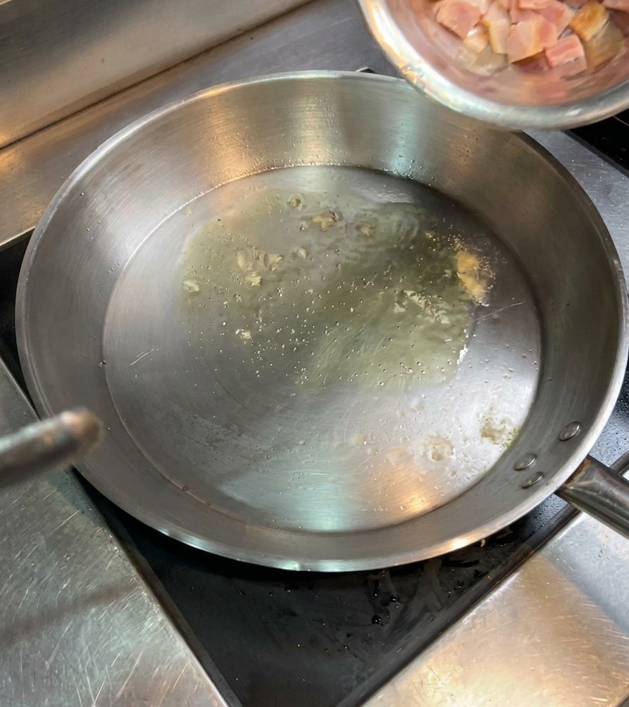 Petits dés de bacon versés depuis un bol en inox dans une poêle avec de lhuile frémissante.